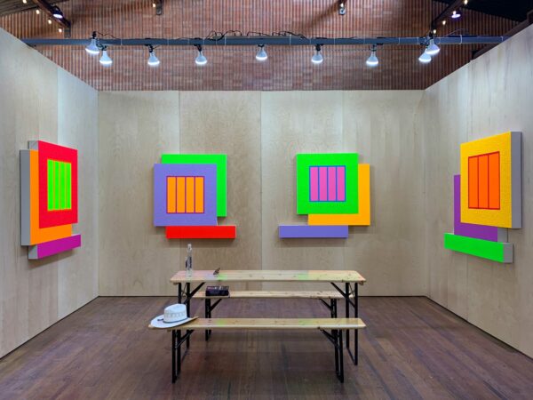 Fluorescent abstract paintings, reminiscent of jail cell windows, are on display in an art fair booth.