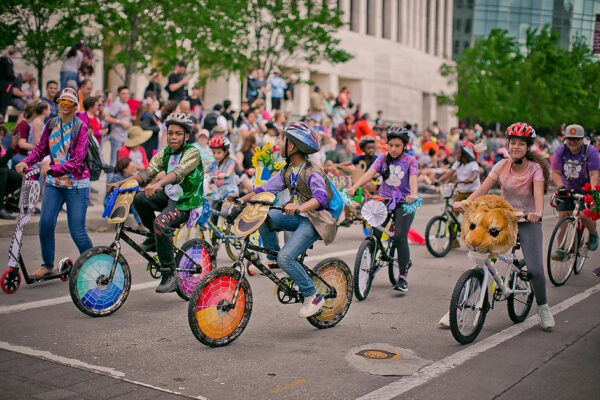 A photograph of a group of school kids riding decorated bicycles in a parade.