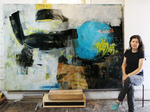 A photograph of artist Tatiana Escallón sitting in front of a large abstract artwork..