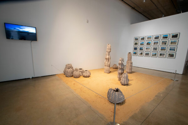Installation view of sculptural object on the floor in sand and photos on a wall