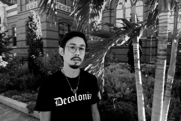 Black and white portrait of Ramon Cardenas wearing a tshirt that says "Decolonize"