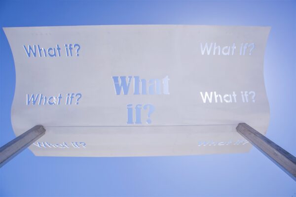 A photograph of one of the steel shade structures installed at Poet's Pointe. The shade has the phrase "What If?" cut out in various fonts.