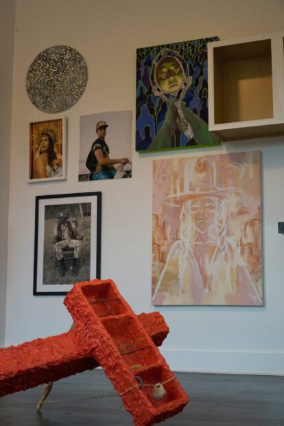 Installation view of two dimensional works on a wall and a red sculpture