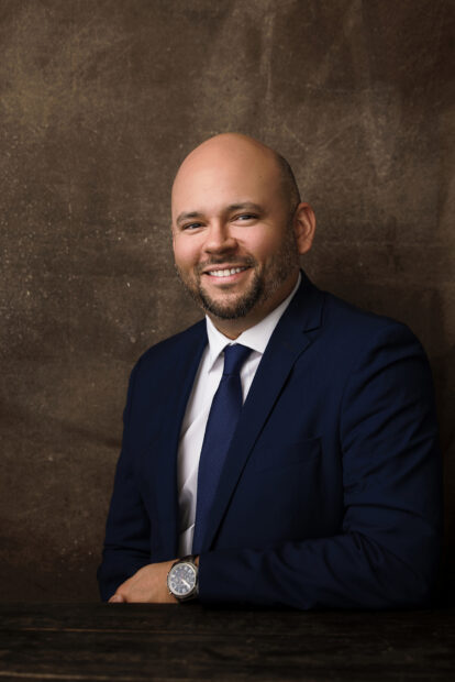 A portrait of a bald, mixed-race man. He is wearing a suit.