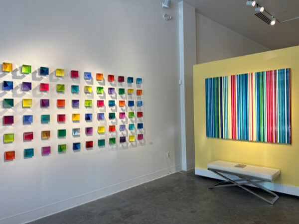 Installation view of cubes on a white wall and a striped painting on a yellow wall