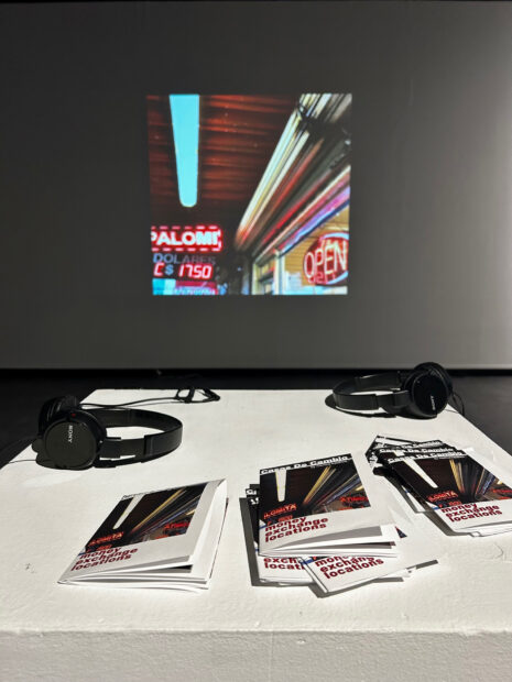 Installation view of a video projection, headphones, and booklets on a pedestal