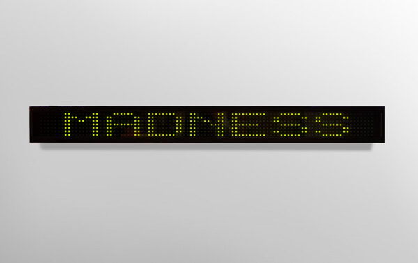 An electronic LED sign with the word "Madness" written in all capital letters. Artwork by Jenny Holzer. 