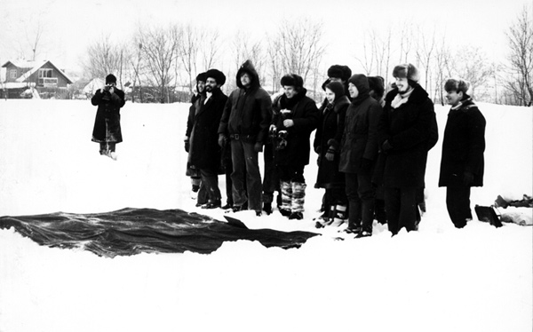 A black and white photograph of a group of people engaging in a performance art action in a snowy field.