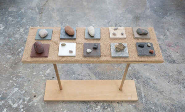 A photograph of an installation of various sized rocks sitting on square tiles.