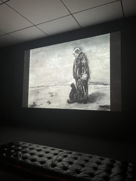 A photograph of an animated film by William Kentridge projected in a dark room.