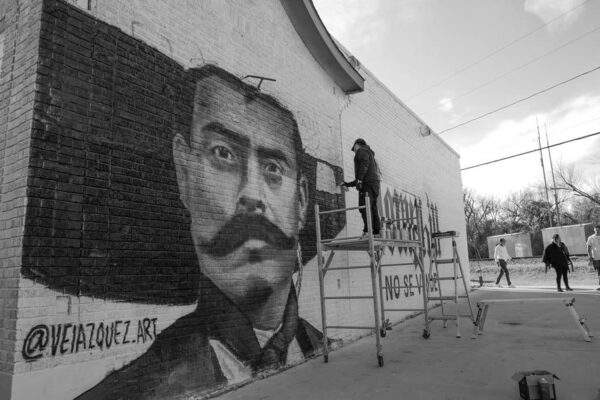 A black and white photograph of Fort Worth-based muralist Juan Velazquez painting the "Hemphill No Se Vende" mural.