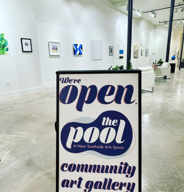 A photograph of a welcoming sign at The Pool, community art gallery, with an exhibition visible in the background.