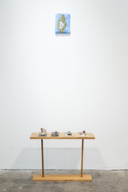 Fresco, champagne silver, river sand, rocks from Scotland, limestone building tiles, oyster shell, pigment, foam are arranged on a short wooden table against a white wall