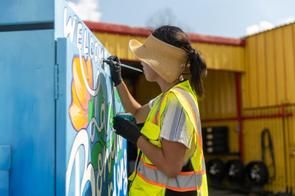 A photograph of Houston artist Caroline Truong painting a Traffic Signal Control Cabinet.