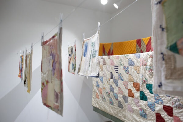 A photograph of an installation of textile works hanging on a clotheslines in a gallery.