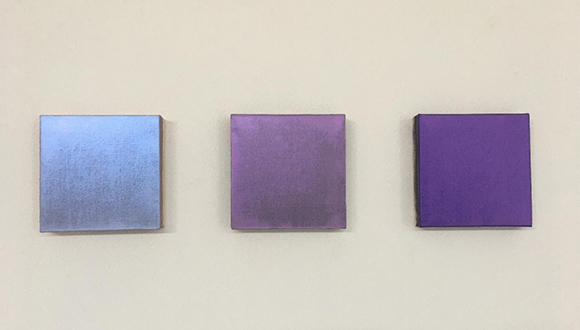 Three iridescent paintings by artist David Simpson hang on a gallery wall.