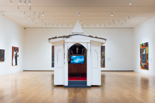 Jammie Holmes, Church in the Wild, 2023 (installation view). Painted wood, shingles, interior acrylic paint, wood paneling, carpet, mid-century modern credenza, books, artificial plants, and color video with sound; 2 minutes, 29 seconds. Overall: 12 × 8 ½ × 11 feet. © Jammie Holmes. Courtesy of the Artist. Photo by Evie Marie Bishop