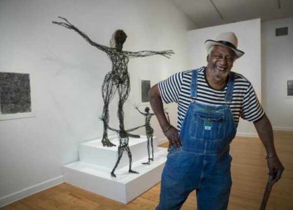 A photograph of Jesse Lott at the Station Museum of Contemporary Art with his wire figure sculptures in the background.