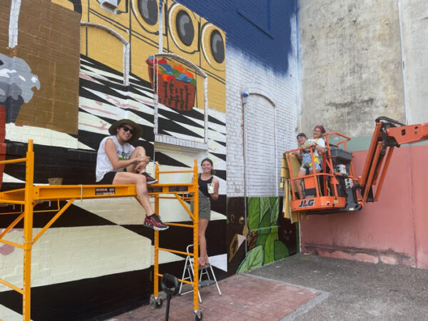 A photograph of a small group of people working on a large scale mural.
