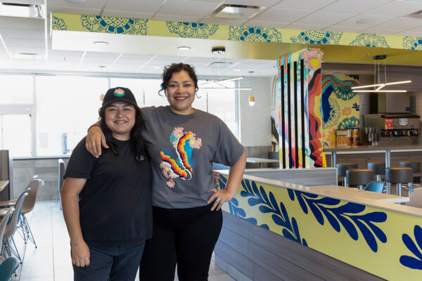 A photograph of muralists Manola and Maria Ramirez standing inside of a McDonald's where they have installed a mural.