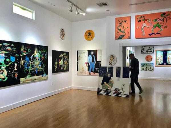 The interior of an art gallery, featuring many colorful paintings.