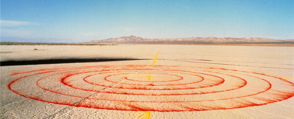 A photograph of a land art work by Lita Albuquerque featuring red pigment placed in concentric circles in a desert.