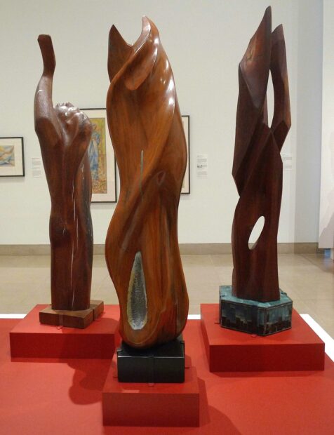 Three wood sculptures standing together on a red base