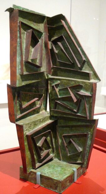 A geometric copper sculpture with green patina