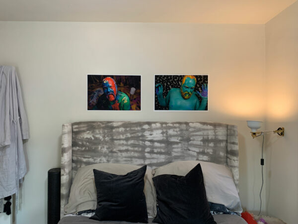 Two photographs of a man whose body is painted different colors are hung above a bed.