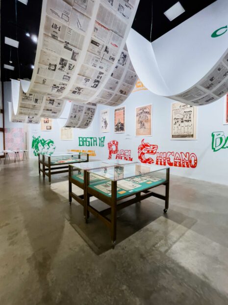 Installation view of El Frente Exhibition with graphics painted on the walls and newspapers hanging from ceilings
