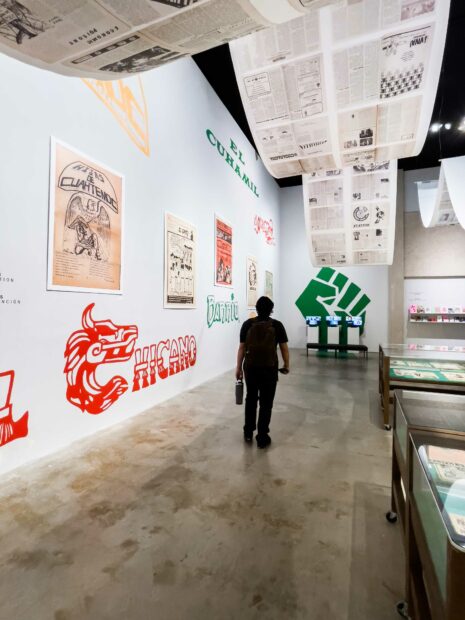 Installation view of painted graphics on a wall and newspapers hanging from a ceiling