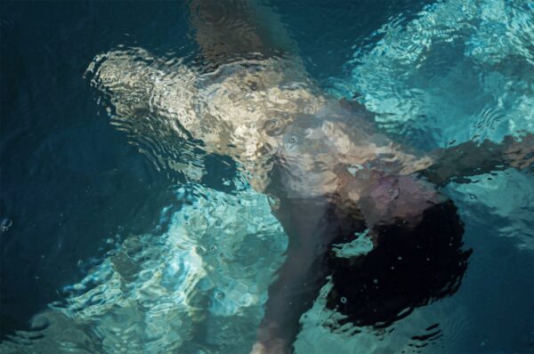 A blurred photograph of a nude female figure immersed in water. 