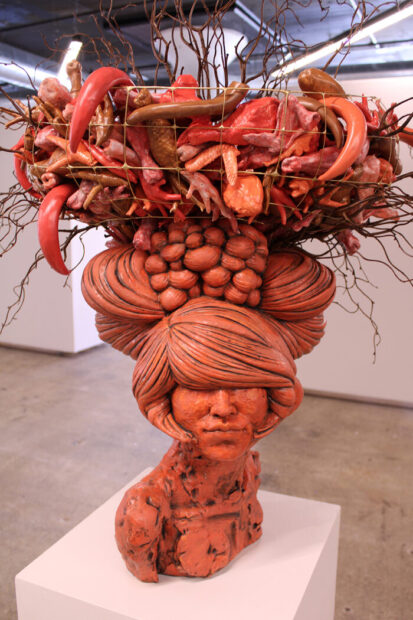 A photograph of a ceramic work by Misty Gamble featuring a woman balancing a large basket on her head.
