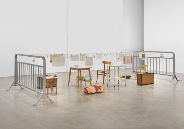 A photograph of an installation by Mona Hatoum featuring furniture and household objects suspended on moving wires.
