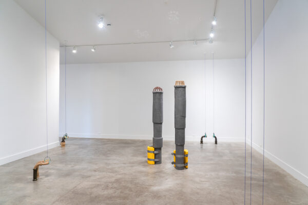 Installation view of two large industrial towers and pipes with wire in a gallery space