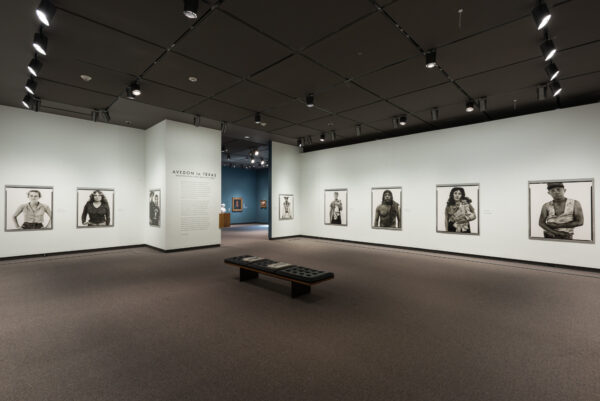 An installation image of the exhibition "Avedon in Texas," featuring several large-scale black and white portraits of people hanging in a white-walled gallery.