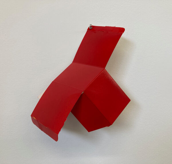 A box covered in red paint is pinned to the wall of a gallery.