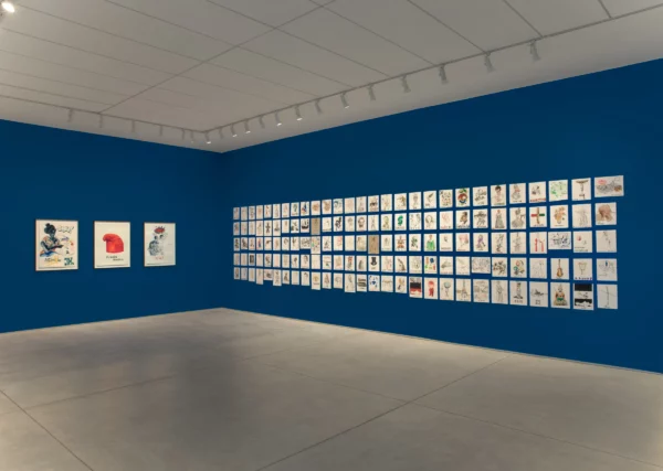 A gallery installation featuring many small artworks hung on top of a royal blue-painted wall.