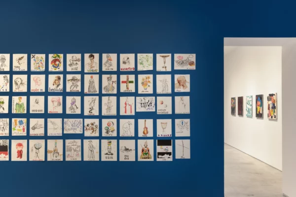 A gallery installation featuring many small artworks hung on top of a royal blue-painted wall.