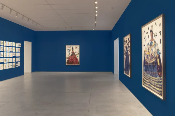 A gallery installation featuring many small artworks and three large artworks on top of a royal blue-painted wall.