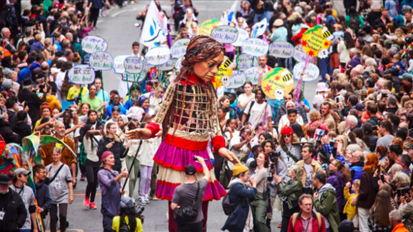 A photograph of a large puppet walking through a crowd of people.