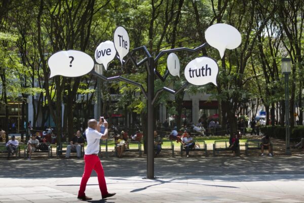 A photograph of a public art work by Hank Willis Thomas of a black tree-like object with white speech bubbles coming off of the branches.