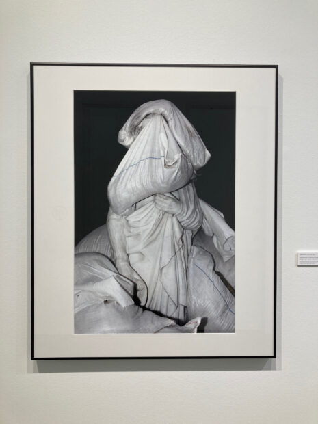 A framed photo of a white statues covered in white sandbags against a black background.