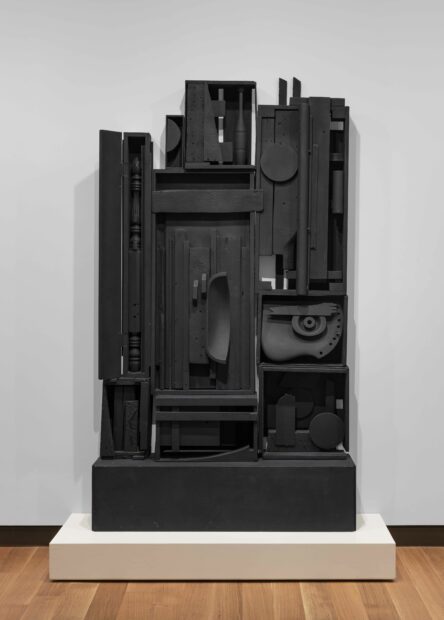 Installation view of a large black Nevelson sculpture on a white plinth
