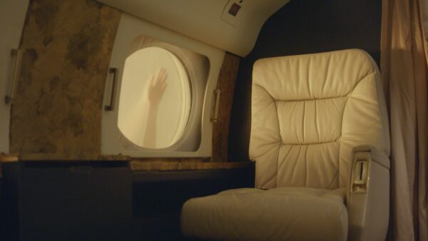 Video still of an empty leather seat on a plane and a hand on the window