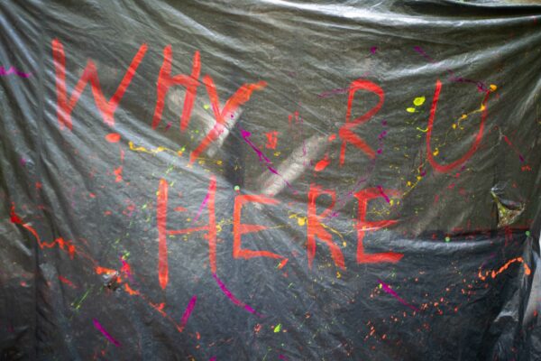 Picture of the words "Why R U HERE" on a black tarp