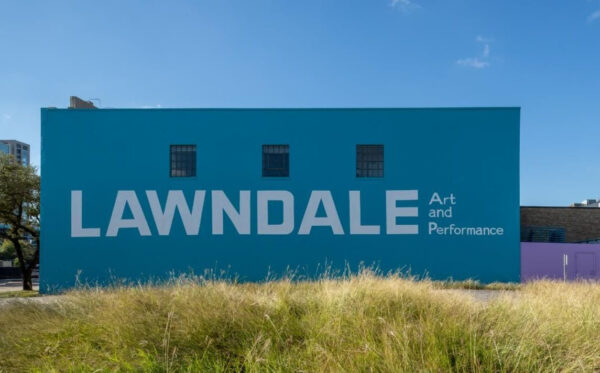 A photograph of a mural of white text on a blue background. The text reads "Lawndale Art and Performance."