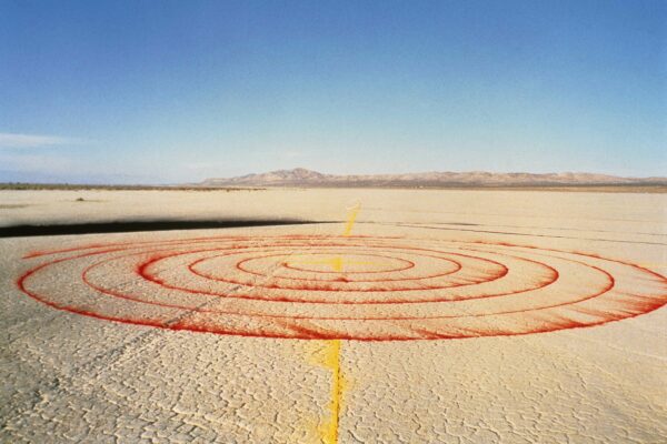 Sobre el suelo desértico está dibujada una espiral roja atravesada por una línea amarilla.