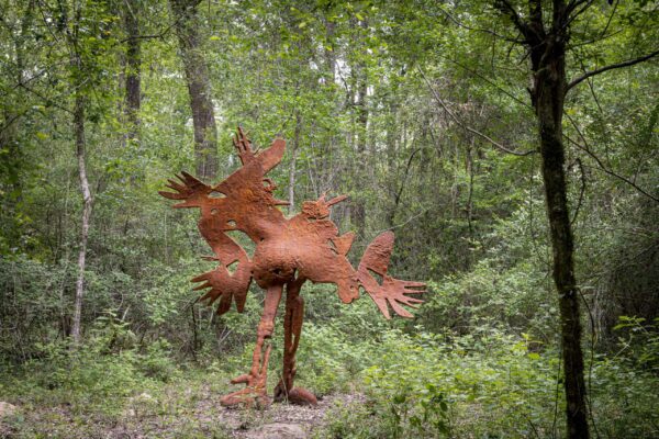 A large sculpture of a bird-like creature, installed in a forest.