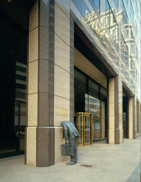 A photograph of a bronze sculpture of a man leaning over with his head appearing to vanish into a wall. Artwork by Terry Allen.